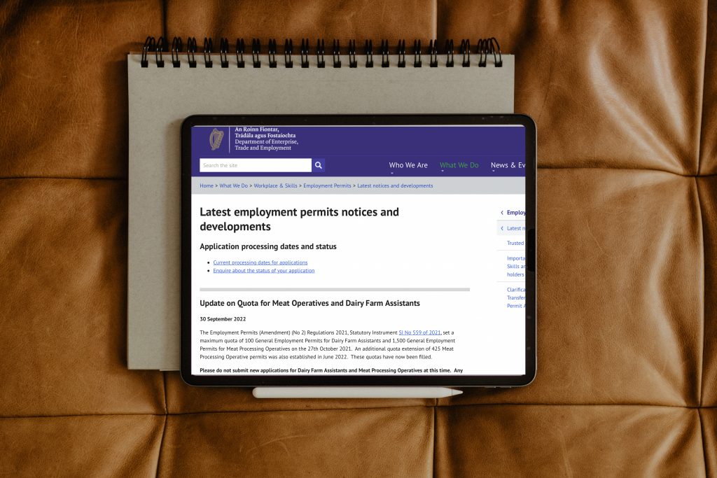 Flatlay of tablet screen displaying Department of Enterprise Trade and Employment website sitting on brown leather with Employment Permits notices 